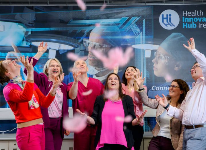 Six women and a man photographed mid-celebration with a Health Innovation Hub Ireland poster behind them.