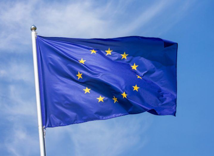 An EU flag with a blue sky and clouds in the background.