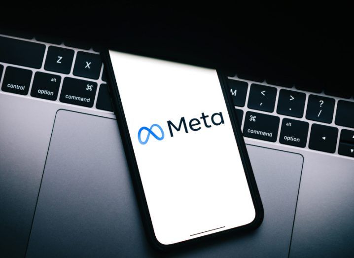 The Meta logo on a smartphone screen, which is laying on a laptop keyboard.