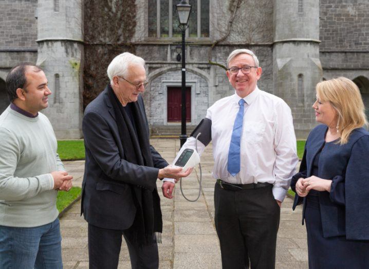 Three men and a woman stand in front of the University of Galway. One of them is wearing a blood pressure monitoring device.