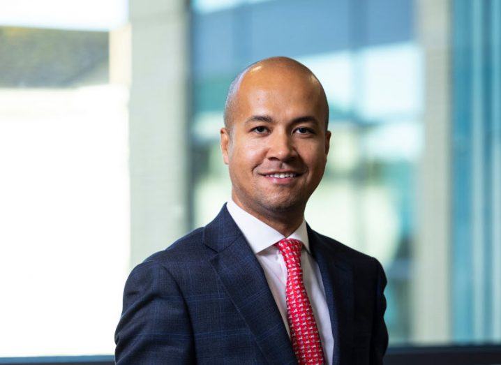 Headshot of Aon's Karl Curran, wearing a suit with a red tie with a window in the background.