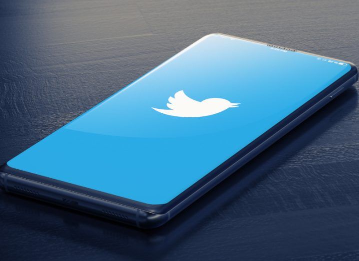 The Twitter logo in a blue background on a smartphone, which is on a dark surface.