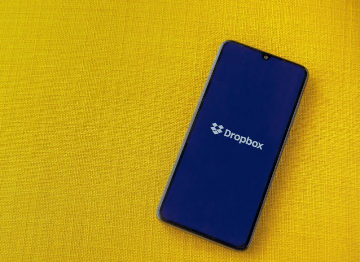 The Dropbox logo on a smartphone screen, lying on a yellow surface.