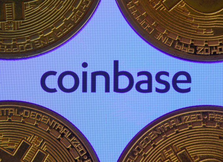 The Coinbase logo on a white surface, with four gold coins next to each corner of the logo.