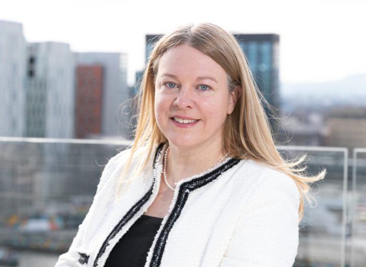 Headshot of online safety commissioner Niamh Hodnett standing on a balcony with a view of the city and buildings behind her.