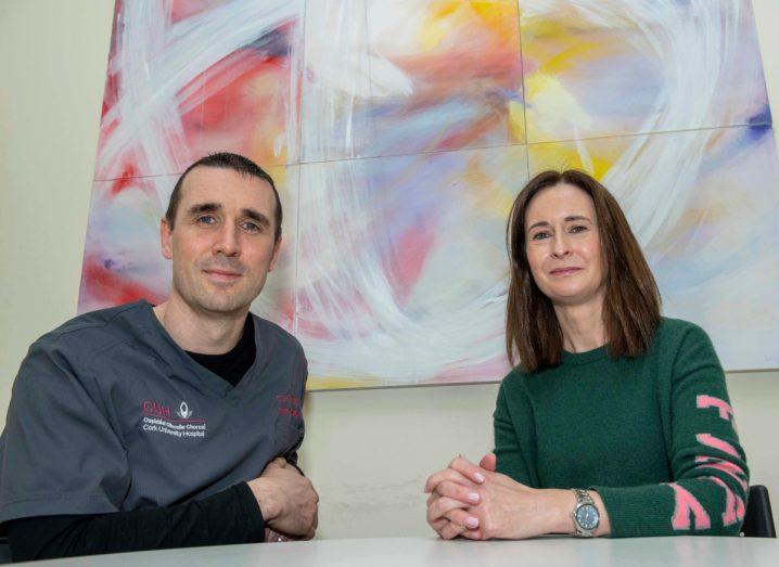 A man and a woman sitting next to each other with a wall painting behind them. Both are involved in calls for support for the Cork University Hospital cancer trial.