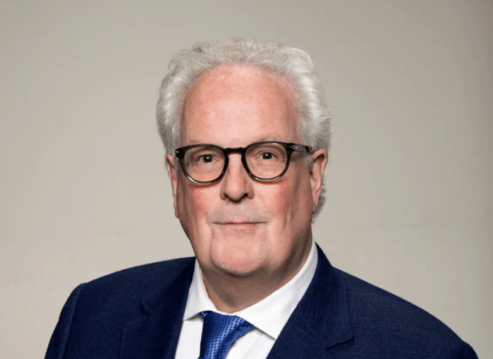 Headshot of a man in a suit, standing in front of a grey brown background. He is Joe Redmond, CEO of Paytrix Ireland.