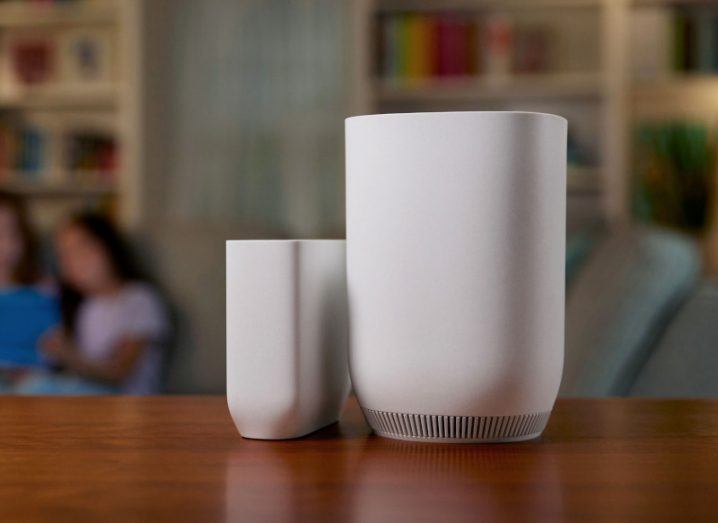 A Comcast Wi-Fi router on a wooden table in a room, with two people sitting in the background.