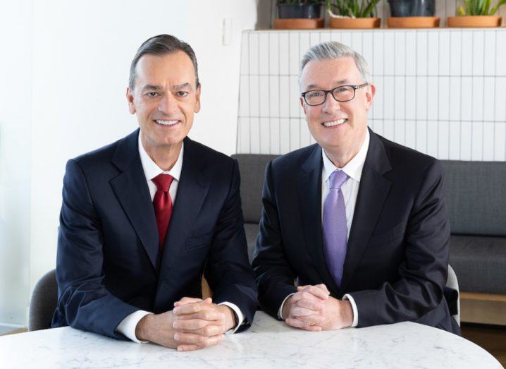 Two men in business formals sitting next to each other.