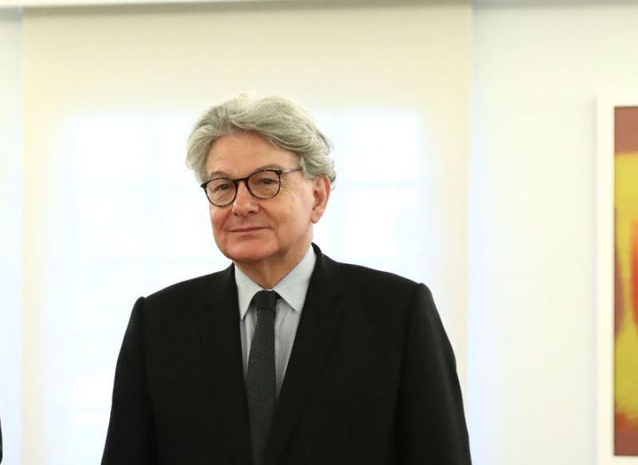 A man in a black suit standing in a room with a white wall behind him. He is Thierry Breton, an EU commissioner.