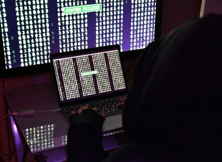 A person in front of two screens that have multiple numbers and 'system failure' written on them. Used as a concept for DDoS attacks.