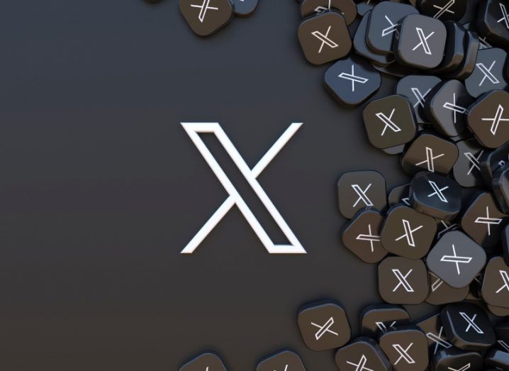 The X logo on a black surface, with a pile of black squares that also have the X logo on the right.