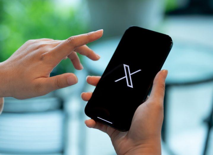 The X logo on a smartphone screen, held in a person's hand.