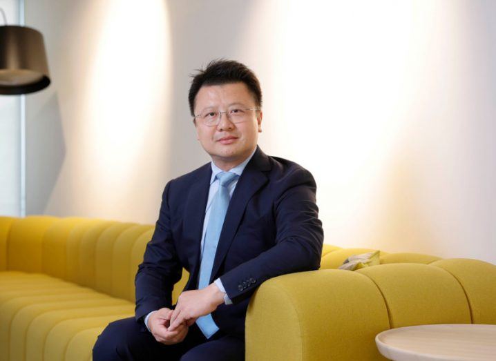 A man in a suit sitting on a yellow couch in a room. He is Calvin Lan, the CEO of Huawei Ireland.