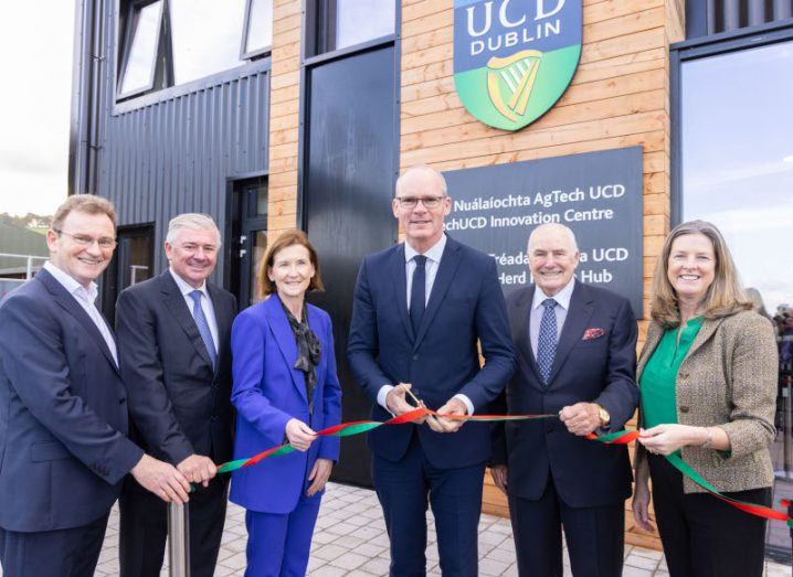 Four men and two women holding a ribbon outside of a UCD building.