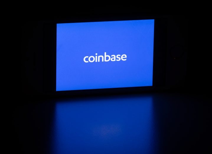 Coinbase logo on a smartphone screen placed in a dark environment.