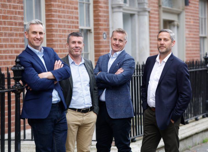 Four men in business formal and casual attire stand next to each other in what appears to be a street in Dublin.