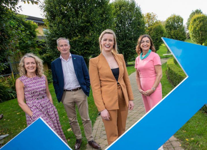 Three women and a man standing by a small path with a blue arrow sign in front of them. They are part of Enterprise Ireland's Going for Growth programme.