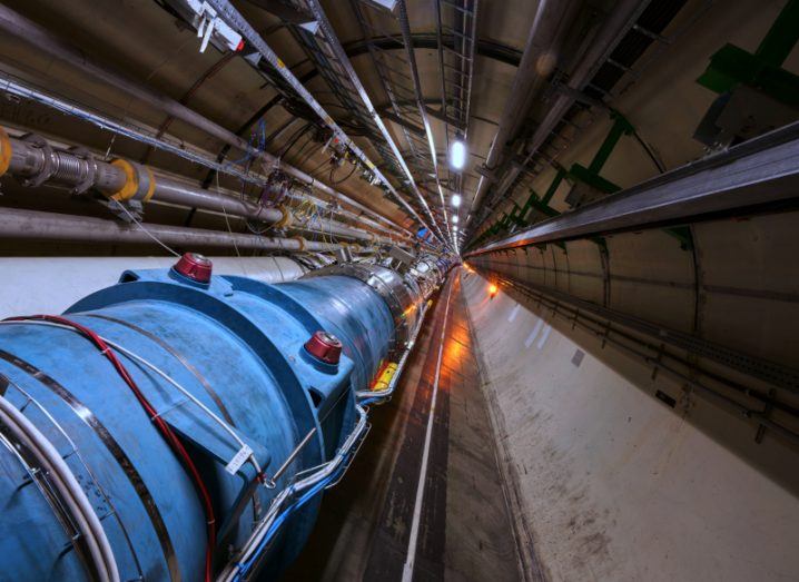 A blue pipe in the centre of a circular room, with grey pipes on the walls. A section of the CERN Large Hadron Collider.