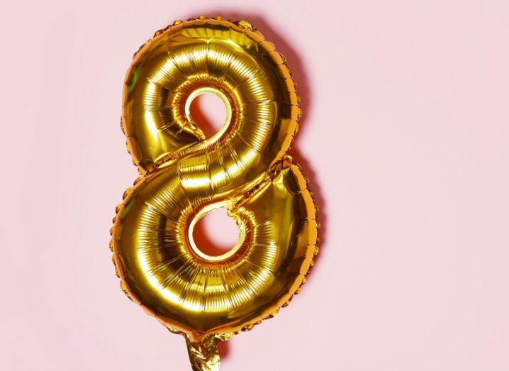 A large gold foil balloon in the shape of the number eight against a pale pink background.