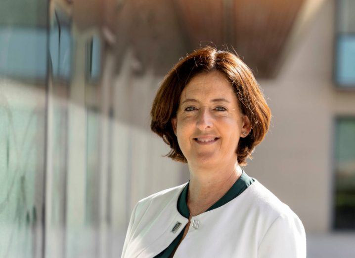 A woman in a white top standing in front of a building with a row of windows to her right. She is Michelle Mullally of Siro.