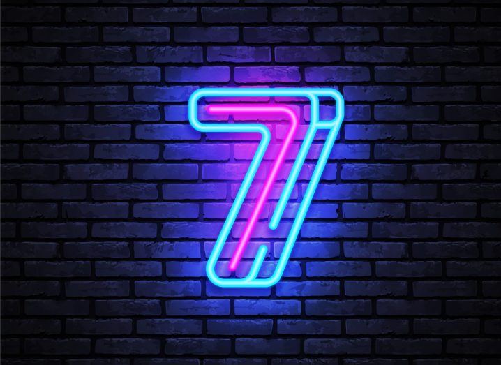 The number seven in shades of neon blue in a dark brick wall background.