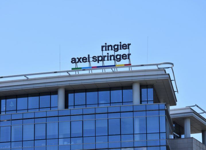 The axel springer logo on the top of a glass building against a bright blue sky.