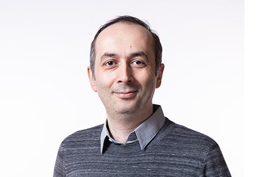 A man in a grey jumper standing in a white background.