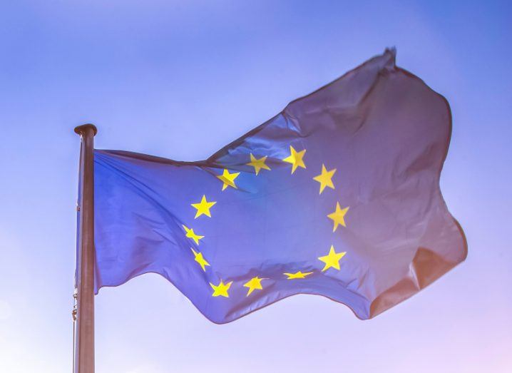 An EU flag flying in the breeze against a blue sky.