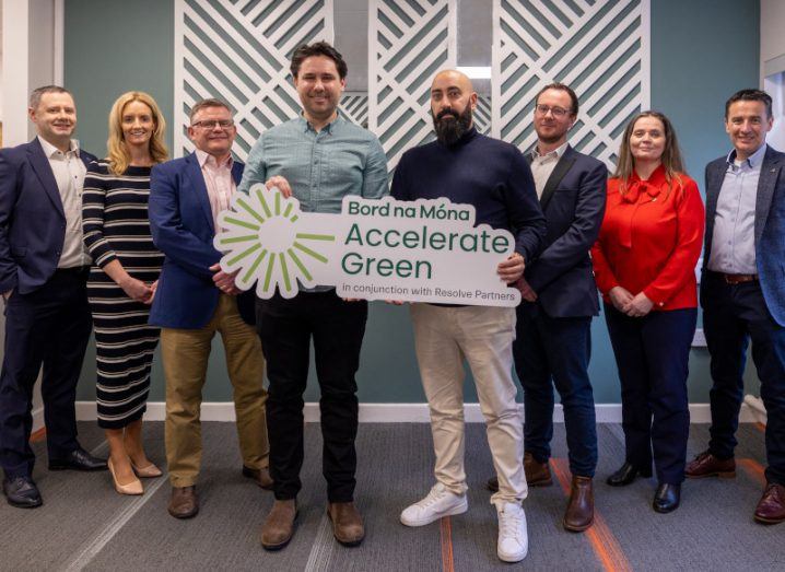 Six men and two women standing in a room, with two of the men holding a Bord na Móna Accelerate Green sign.