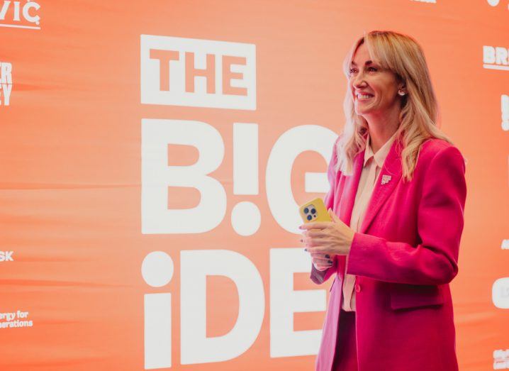 A woman stands in front of a display that reads The Big Idea. She is looking away from the camera and smiling.