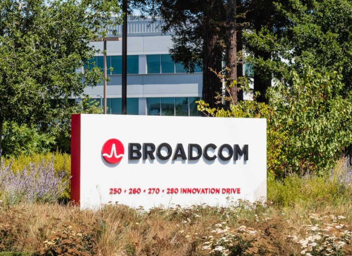 A white and red sign with the Broadcom logo on it displayed outside a large office building.