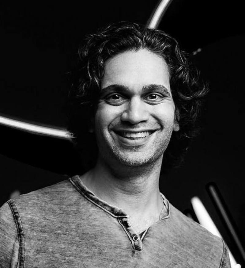 Black and white headshot of Aaron Rodericks smiling at the camera.