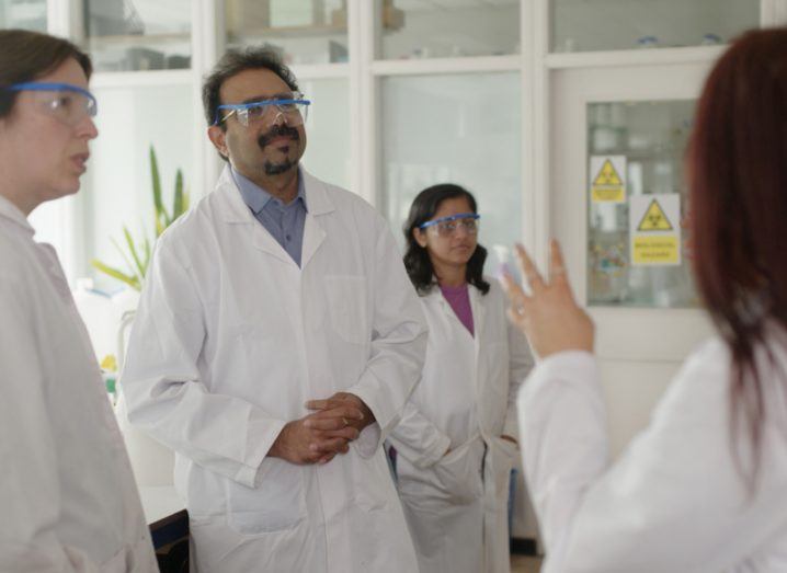 A group of researchers in white lab coats speaking in a room.