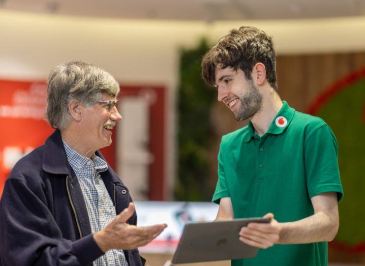 Two men talking together with one of the men wearing a green shirt with a Vodafone logo on it.