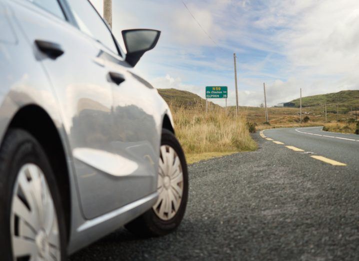 A grey car on a road in Ireland, with a green sign ahead.