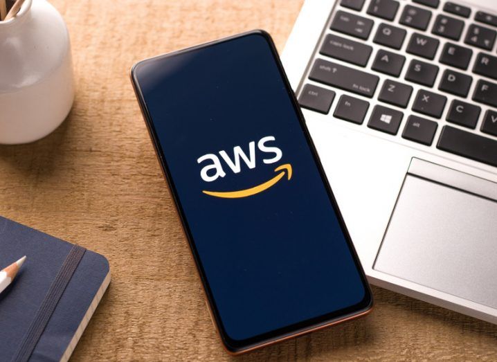 The AWS logo on a smartphone screen, which is laying on a wooden table.