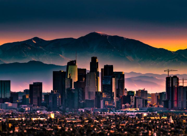 Skyline of Los Angeles with mountains in the backdrop during sunrise.