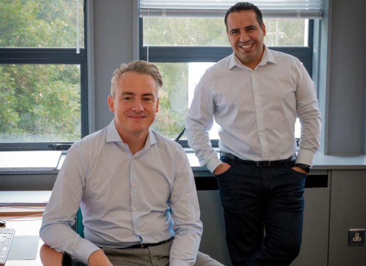 Two men in an office room, one seated and one standing.