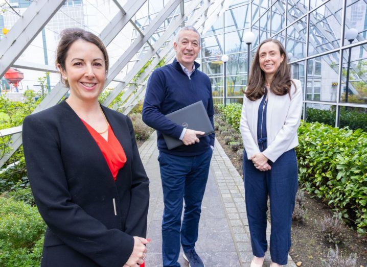 Two women and a man stand inside what appears to be a greenhouse.