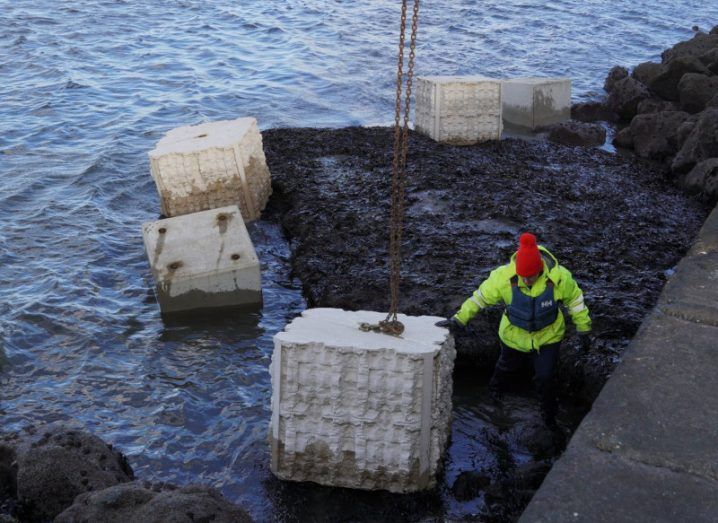 A person standing on the shore of Dublin Port with 3d-printed units lying around.