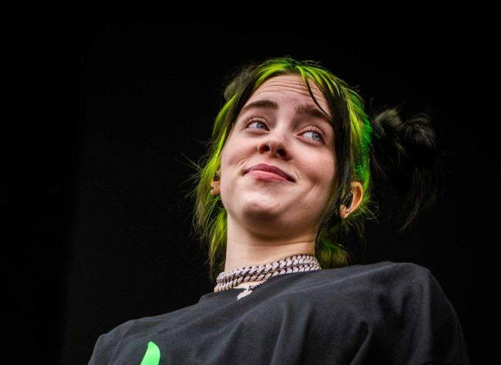 Billie Eilish standing on a stage in a black background.