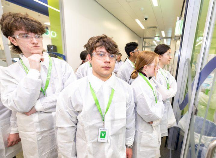 Multiple students in white lab outfits in a hallway. Two of the students are winners of a BT Young Scientist and Tech Exhibition Regeneron award.