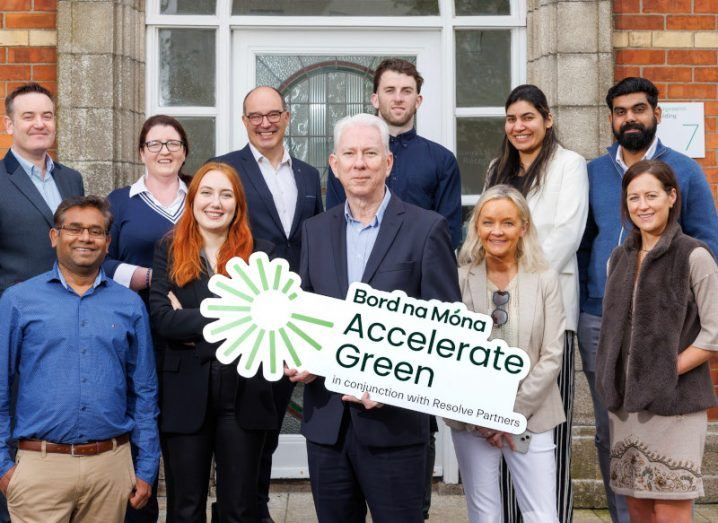 A group of men and women standing in front of a building. One man is holding a sign for the Bord na Móna Accelerate Green programme.