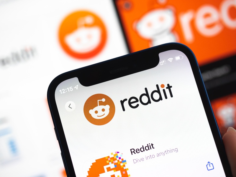 The Reddit logo on a smartphone screen and on screens in the background.