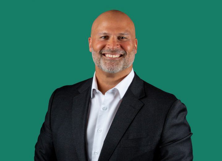 A man wearing a black suit with a white shirt smiles at the camera in front of a dark green background. He is Ravi Malick, SVP and global CIO at Box.