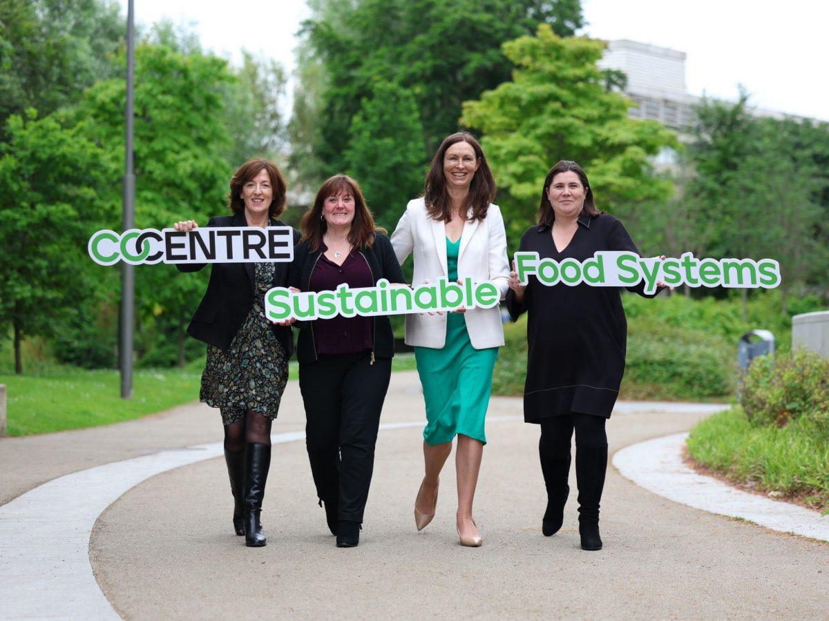 Four women walking down a road holding signs that read "Co-centre Sustainable Food Systems".
