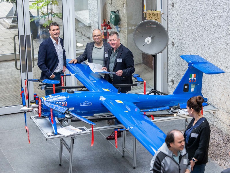 Men and women stand around a model of the Guard drone, which looks like a small blue plane.