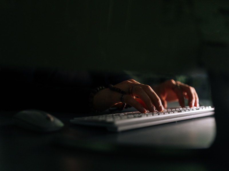 Person typing on a keyboard in front of a screen in a dark room.