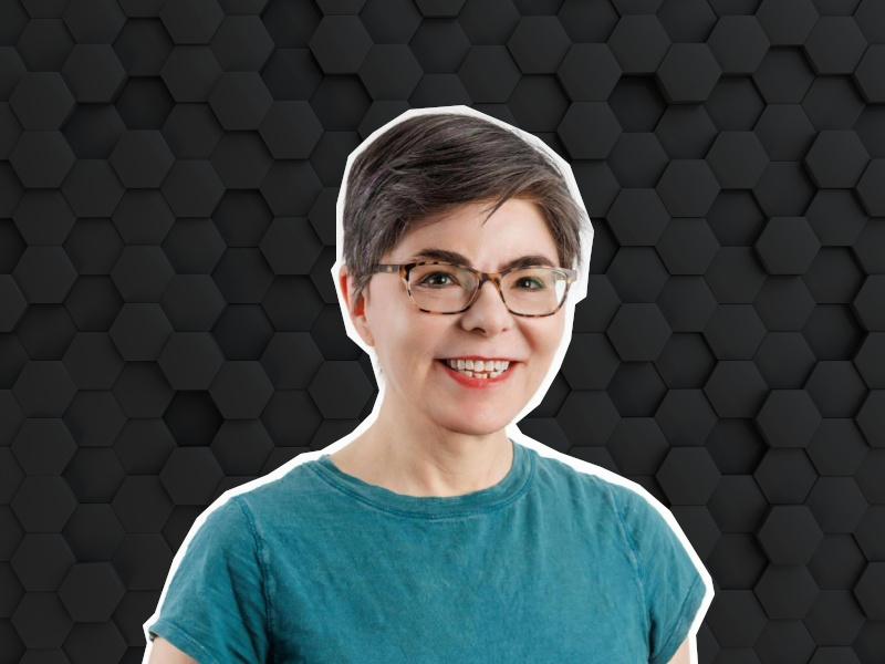 A woman wearing a turquoise shirt and glasses smiles at the camera over a digital background made of black hexagonal shapes. She is Diana Kelley, the chief information security officer at Protect AI.